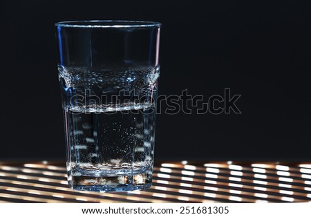 Glass of clean mineral water on lattice surface and dark color background