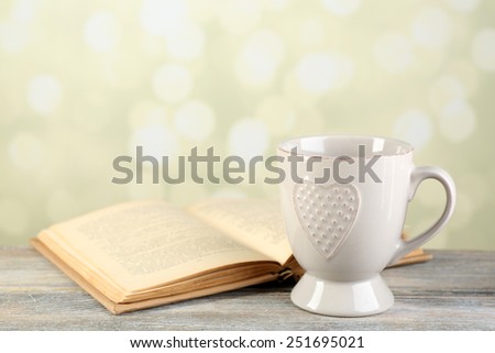 Cup of tea and book on table, on light background