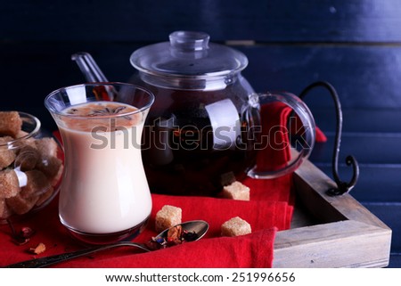 Black tea with milk and lump sugar on wooden tray with napkin and color wooden planks background
