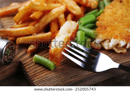 Breaded fried fish fillet and potatoes with asparagus on wooden cutting board background