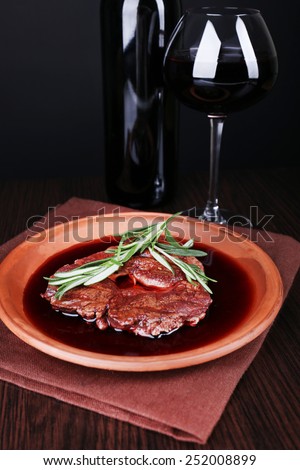 Grilled steak in wine sauce with glass of wine on dark background