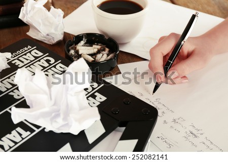 Female hand writing script at desktop with moving clapper and sheets of paper background