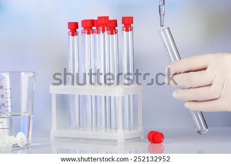 Hand of assistant with liquid in test tubes during experiment in laboratory on light blurred background