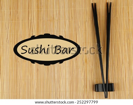 Pair of chopsticks and Sushi Bar text on bamboo mat background