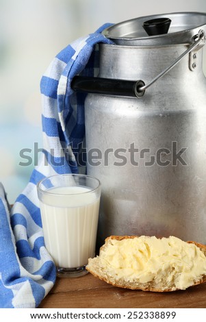 Retro can for milk with fresh bread and glass of milk on wooden table, on light background. Bio products concept