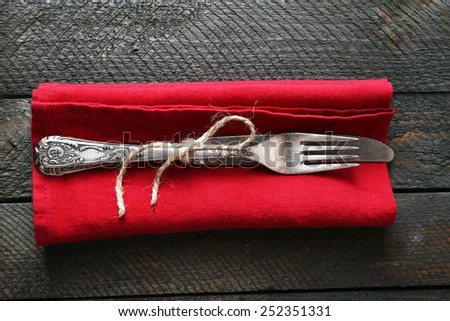 Silverware tied with rope on red napkin on wooden planks background
