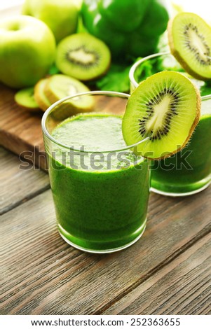 Green fresh healthy juice with fruits and vegetables on cutting board and wooden table background