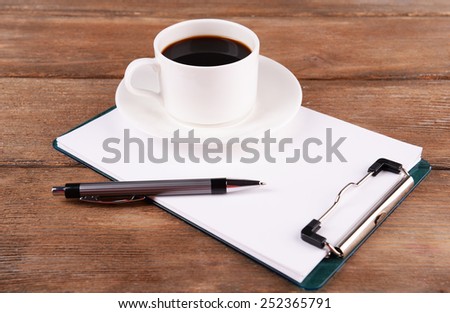 Cup of coffee on saucer with sheet of paper and pen on wooden table background