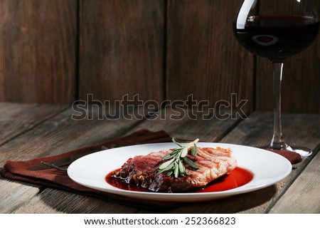 Grilled steak in wine sauce with glass of wine on wooden background