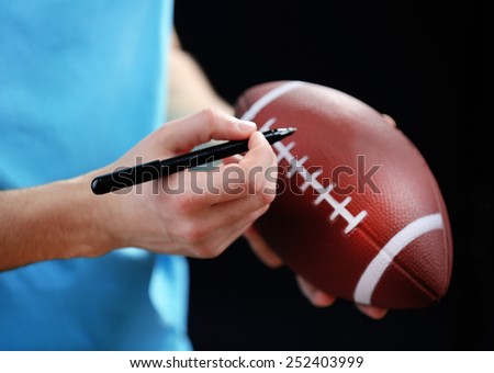 American football star signing autograph on ball on black background