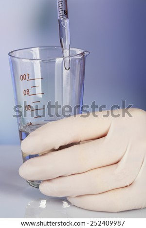 Hand of assistant with liquid in glassware during experiment in laboratory on light blurred background