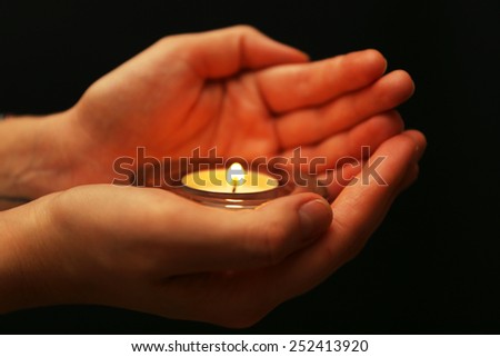 Burning candle in hands on dark background