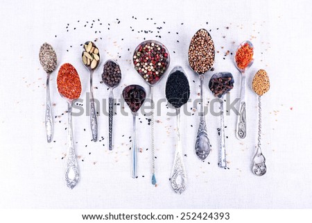 Seasonings in metal spoons on light fabric background