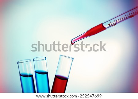 Pipette adding red fluid to the one of test-tubes on bright background