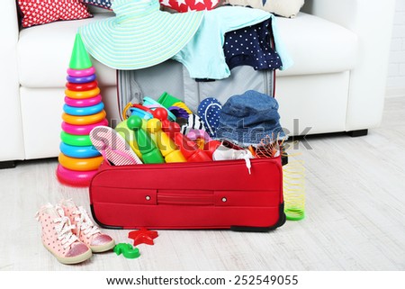 Suitcase packed with clothes and child toys on wooden floor and white sofa background