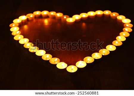 Burning candles in shape of heart on dark background