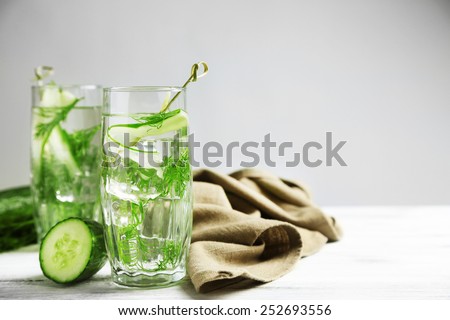 Glasses with fresh organic cucumber water on wooden table, on grey background