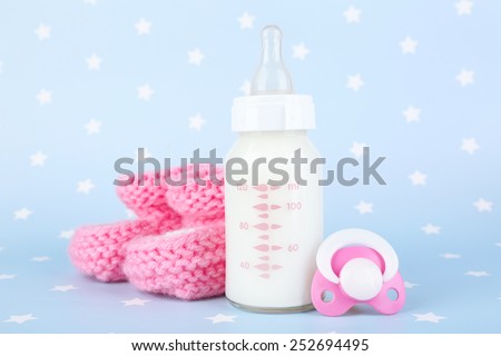 Baby milk bottle, pacifier and babys bootees on blue background