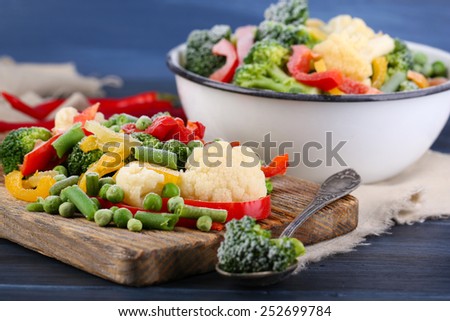 Frozen vegetables on cutting board, on napkin, on wooden table background