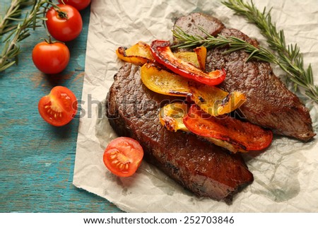 Composition with tasty roasted meat on paper sheet, tomatoes and rosemary sprigs on wooden background