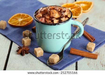 Cup of hot coffee with marshmallow on napkin with lump sugar, cinnamon, star anise and dried orange on color wooden table background