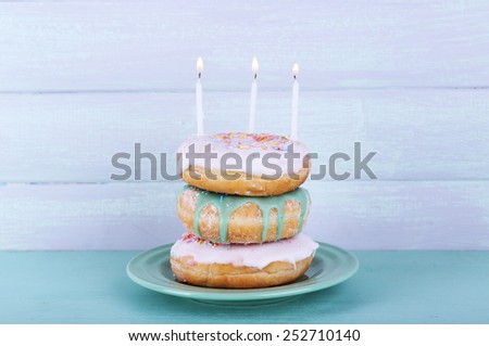 Delicious donuts with icing and birthday candles on table on wooden background