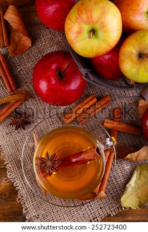Composition of  apple cider with cinnamon sticks, fresh apples and autumn leaves on wooden background