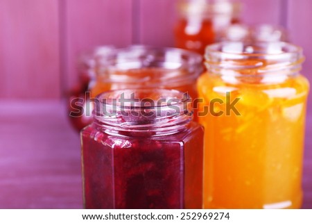 Homemade jars of fruits jam on color wooden background