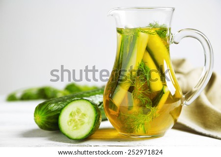 Glass ewer with fresh organic cucumber water on wooden table, on grey background