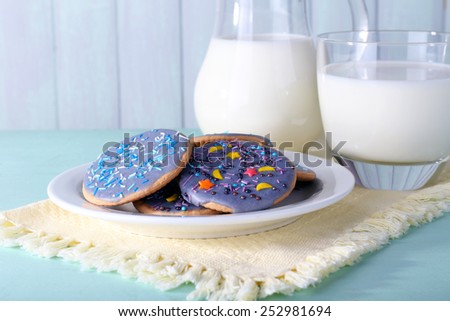 Glazed cookies with glass and jug of milk on color wooden background