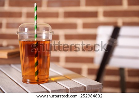 Apple juice in fast food closed cup with tube on wooden table and brick wall background