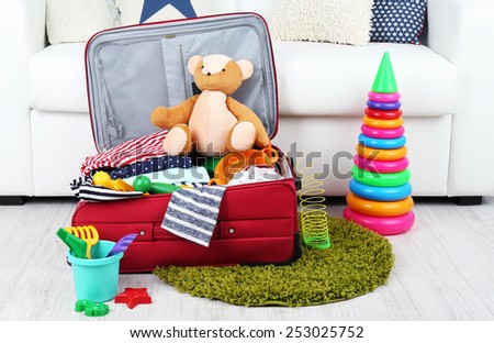 Suitcase packed with clothes and child toys on fur rug and white sofa background