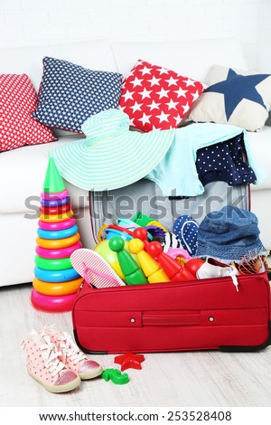 Suitcase packed with clothes and child toys on wooden floor and white sofa background