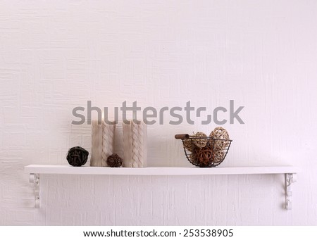 Still life with candles and dried balls on shelf on white wall background
