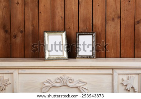 Photo frames on chest of drawers, on wooden wall background