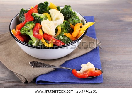 Frozen vegetables in bowl on napkin, on wooden table background