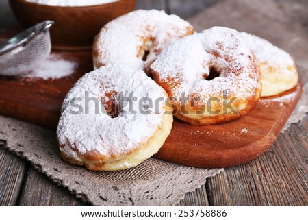 Delicious donuts with icing and powdered sugar on wooden background