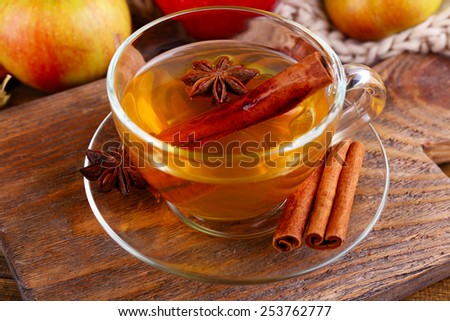 Composition of  apple cider with cinnamon sticks, fresh apples, warm scarf and autumn leaves on wooden background