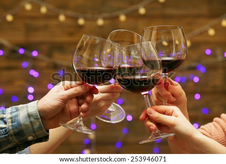 Clinking glasses of red wine in hands on bright lights background