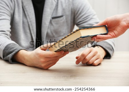 Author signing autograph in own book at wooden table on white planks background