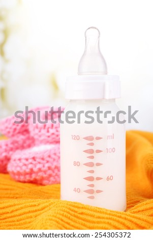 Baby milk bottle and babys bootees on yellow background