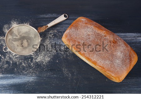 Loaf of freshly bread with strainer of flour on color wooden table background
