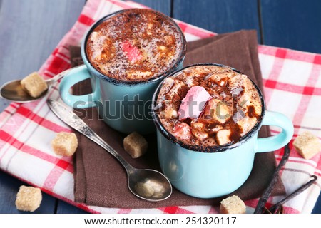 Mugs of hot coffee with marshmallow on napkin with lump sugar, star anise and vanilla sticks on color wooden table background