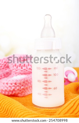 Baby milk bottle, pacifier and babys bootees on yellow background