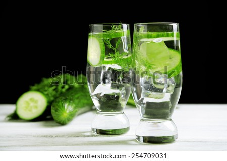 Glasses with fresh organic cucumber water on wooden table, on black background