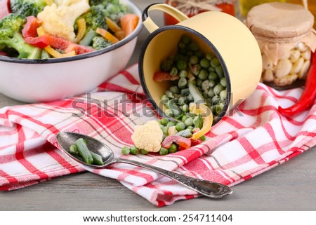 Frozen vegetables in bowl and mug on napkin, on wooden table background