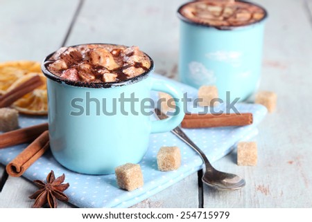 Mugs of hot coffee with marshmallow on napkin with lump sugar, cinnamon, star anise and dried orange on color wooden table background