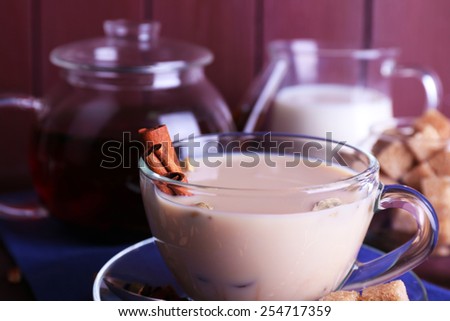 Black tea with milk and lump sugar and spices  in glassware on color wooden planks background