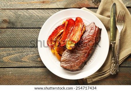 Composition with tasty roasted meat and vegetables on plate, on wooden background