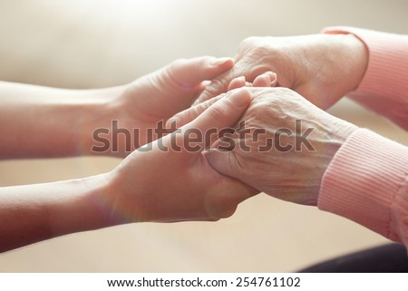 Old and young holding hands on light background, closeup